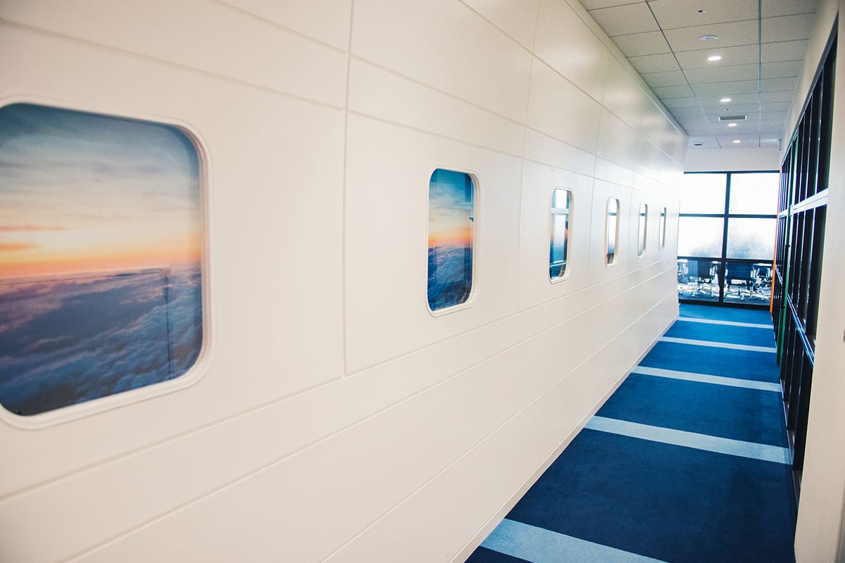 新オフィスには、機内をイメージした廊下もある。エボラブルアジアは自社ウェブサイト、アプリの展開、他社との提携も積極的に行っており、幅広くビジネスを展開している。オフショア開発の拠点としてベトナムに現地法人子会社を置き、現地で独自のシステムの開発・運用を行う。