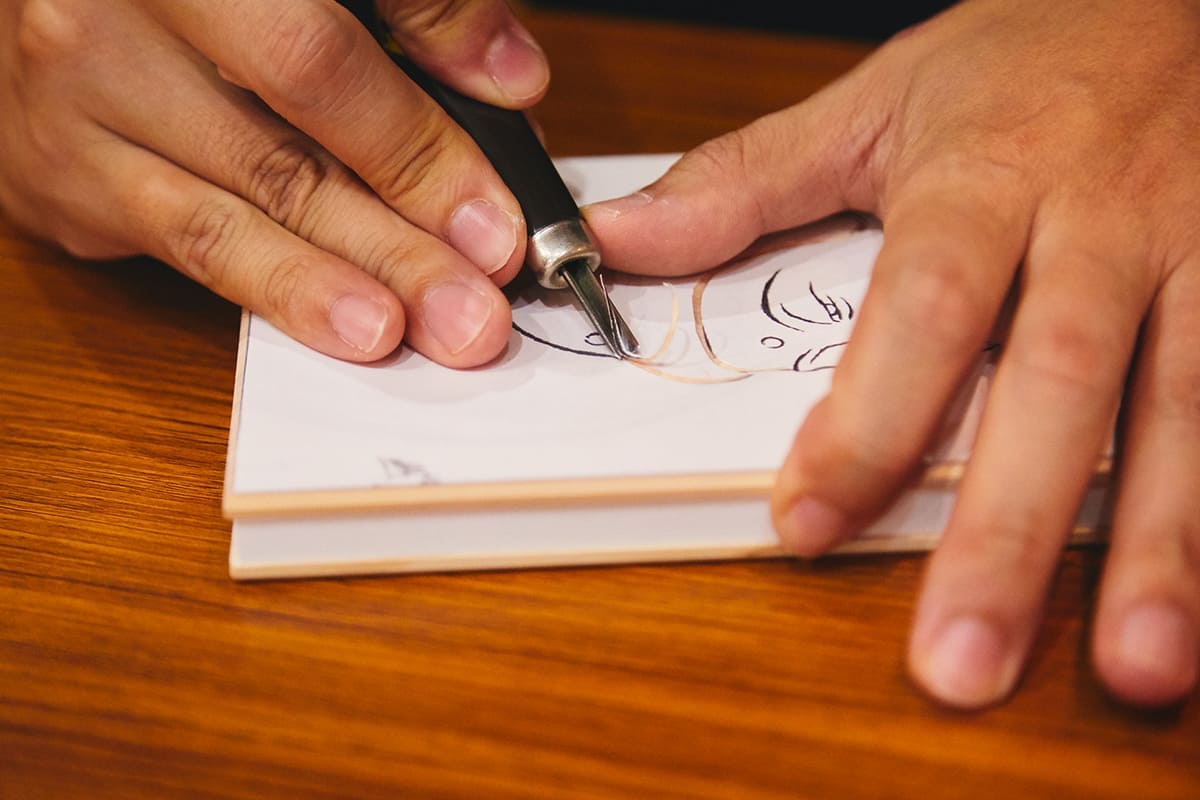 仏像材にも使う檜(ヒノキ)板を使用した御朱印帳の表紙に、プリントされたモチーフを彫っていく。この阿弥陀如来のほかに、蓮の花など仏教にちなんだ絵から選べる。